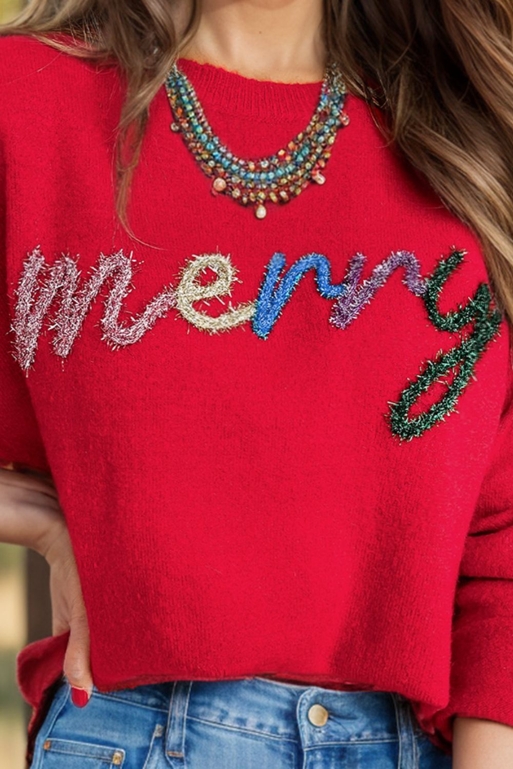 red sweater saying merry in colorful cursive letters looking like tinsel