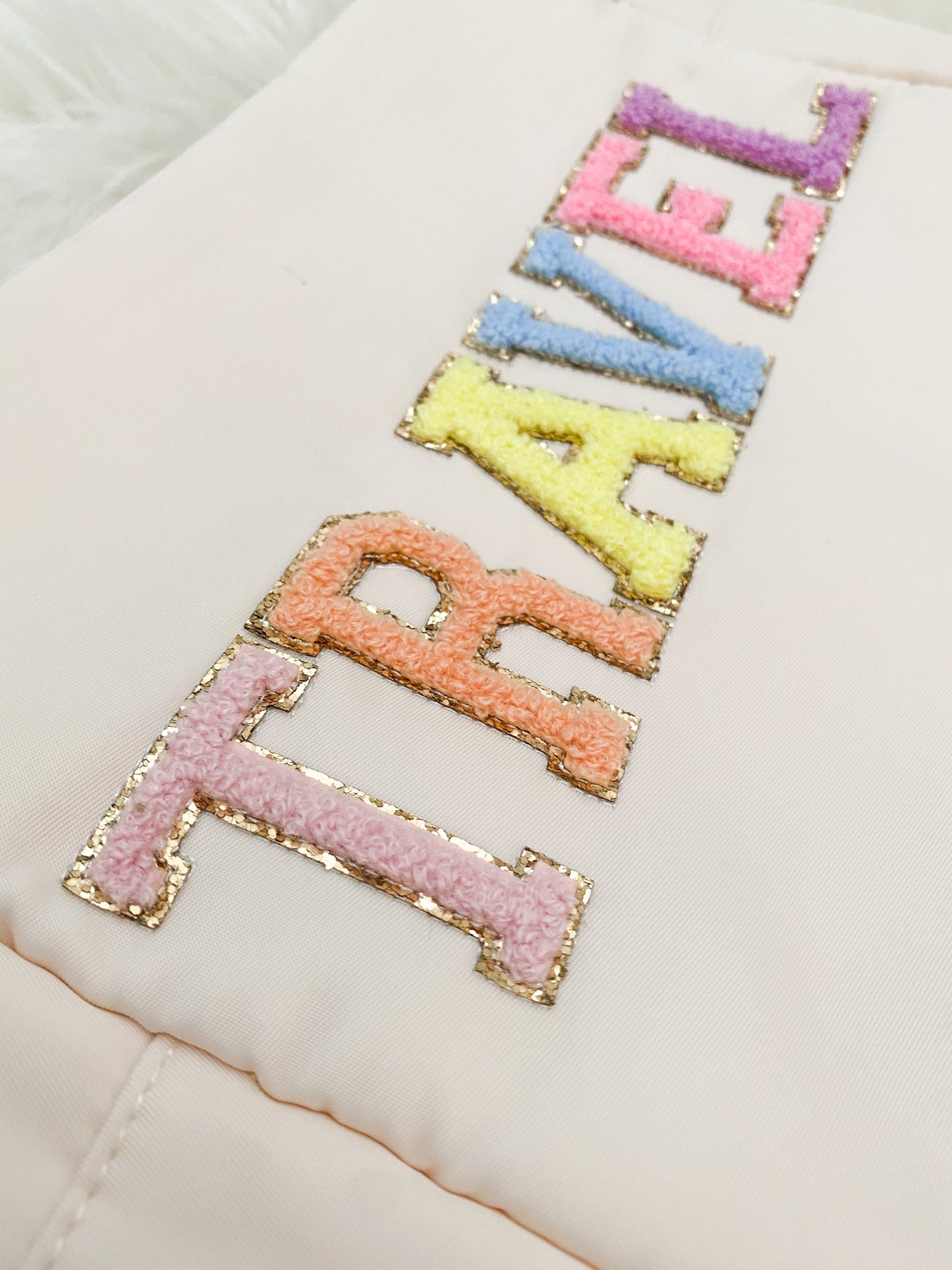 close up of embroidered chenille patches saying "travel" in rainbow letters