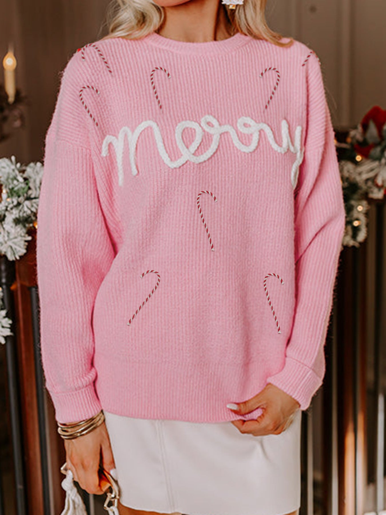 woman wearing pink sweater with embroidered wording merry and candy canes